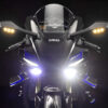 Front view of the 2025 Yamaha YZF-R1M motorcycle. Superbike with blue accents, headlights on, and carbon fiber details.
