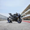 2025 Yamaha YZF-R1M: black and blue sportbike on a racetrack, showcasing its aerodynamic design and high-performance features.