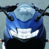 Front view of the SUZUKI GIXXER SF 250 2024 motorcycle in blue on a road, featuring its sleek handlebars, mirrors, and headlights.