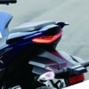 Close-up of a SUZUKI GIXXER SF 250 2024 motorcycle's rear, highlighting the sleek seat, taillight, and turn signals against a blurred road background.