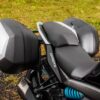 Close-up of a CFMOTO 650 GT ABS motorcycle seat and rear storage boxes, set on gravel with grass in the background.