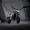 The CFMOTO 800NK SPORT, with its sleek silver and black design, is parked on a dark surface, set against angular concrete architecture.