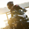 A person in motorcycle gear sits on a stationary CFMOTO 800NK SPORT at a sunlit track, looking to the side.