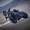 Wearing protective gear, a motorcyclist leans sharply while cornering on a CFMOTO 800NK SPORT at a racetrack, with the blurred background highlighting the thrill of speed.