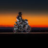 A rider in stylish CFMOTO gear sits confidently on their 800NK SPORT motorcycle, its bright headlight cutting through the vibrant sunset hues.