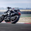 A person expertly leans into a corner on the racetrack while riding a sleek black CFMOTO 800NK SPORT motorcycle.