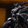 Close-up of a black and white CFMOTO 800NK SPORT motorcycle, emphasizing its front section, handlebars, and tire against a dark background.