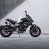 The CFMOTO 800NK SPORT, showcasing a sleek, modern design in gray and black with red accents, is parked on a concrete surface against a large plain wall.