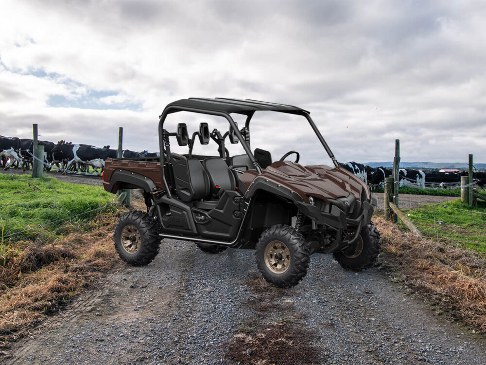 A YAMAHA VIKING SE is parked on a gravel path while cows graze in a field behind a fence under a cloudy sky.