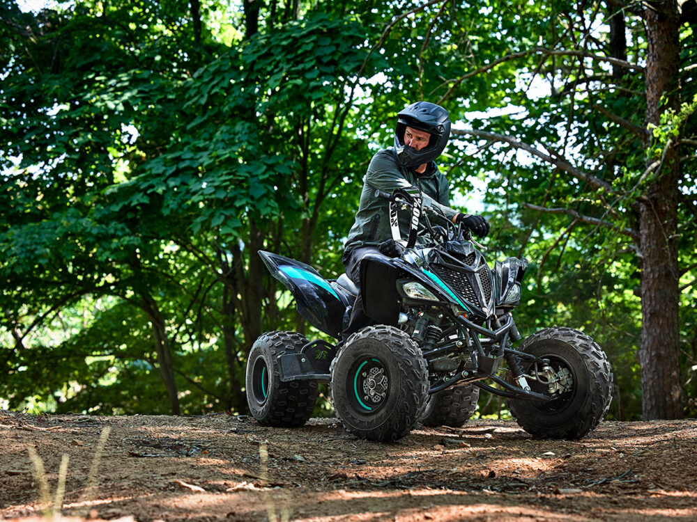 A person riding the 2024 YAMAHA YFM700R ATV navigates through a forest, wearing a helmet.