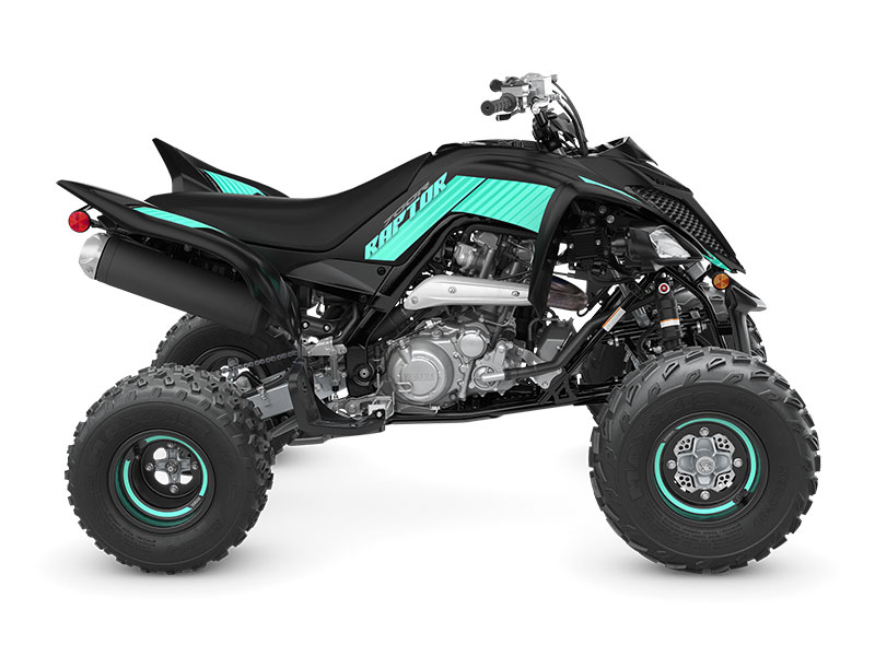 A side view of the YAMAHA YFM700R - 2024, a black and turquoise ATV with large off-road tires and exposed engine components.