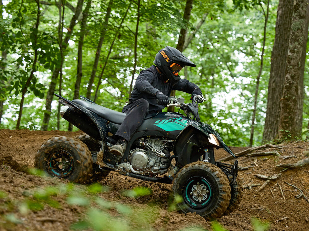 A rider wearing black gear navigates a dirt trail in the forest on a 2024 YAMAHA YFZ450R ATV.