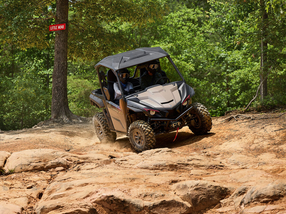 The YAMAHA WOLVERINE X2 XT-R, an off-road vehicle for two passengers, navigates rocky terrain in a forested area with a "Little Moab" sign in the background.