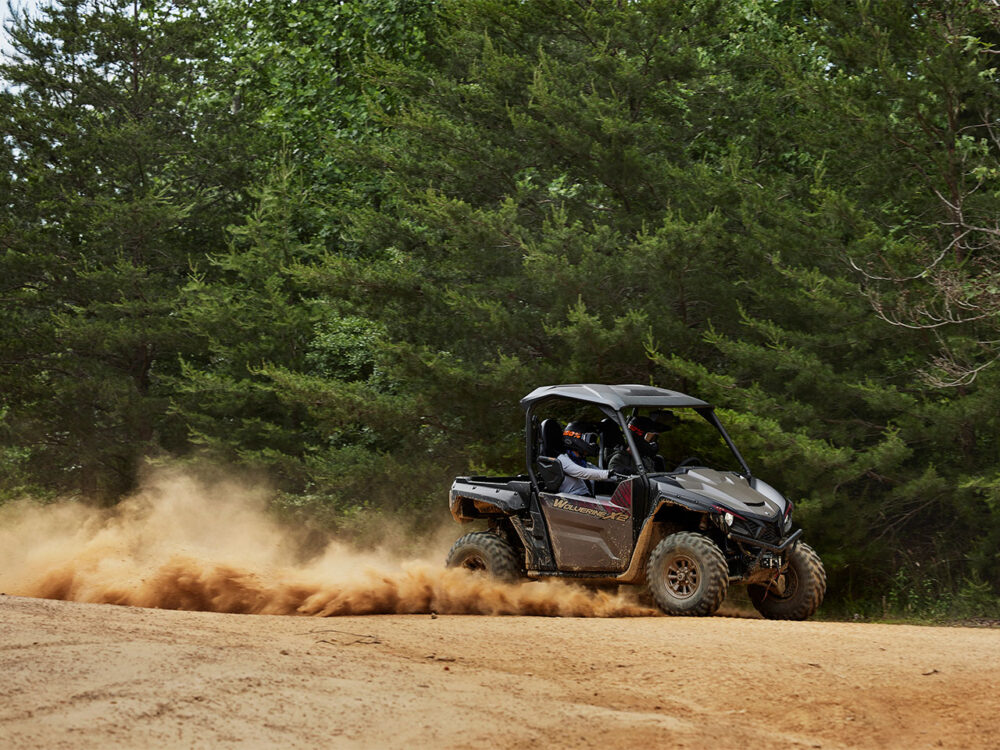 The YAMAHA WOLVERINE X2 XT-R ATV kicks up dust as it navigates a dirt path surrounded by dense green trees.