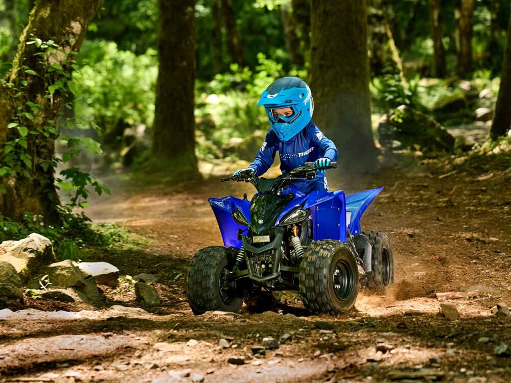 A person wearing a blue helmet and riding gear is driving a YAMAHA YZF50 2025 on a forest dirt trail.