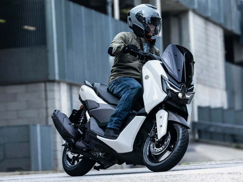 A person rides a YAMAHA NMAX 155 LAMS scooter on the street, sporting a helmet and a khaki jacket.