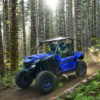 A YAMAHA WOLVERINE RMAX2 1000 SPORT navigates a dense forest trail, kicking up dust as sunlight filters through the trees.