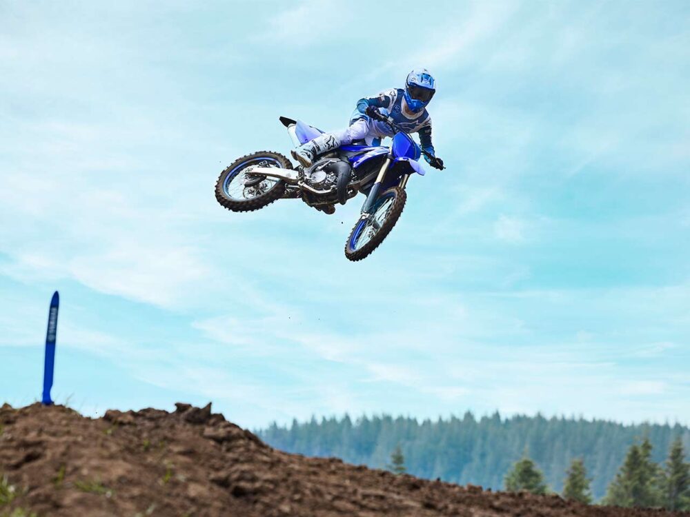 A motorcyclist in blue gear performs a jump on a YAMAHA YZ125 2025 dirt bike against a backdrop of blue sky and distant trees.