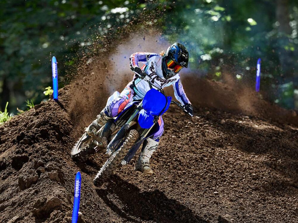 A motorcyclist on a YAMAHA YZ125 2025 rides a dirt track, kicking up dust in their wake, wearing a helmet and protective gear.