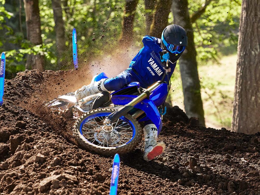 A rider, sporting blue Yamaha gear, expertly maneuvers a YAMAHA YZ125 2025 on a dirt track, kicking up soil as they lean into a turn amidst the trees.