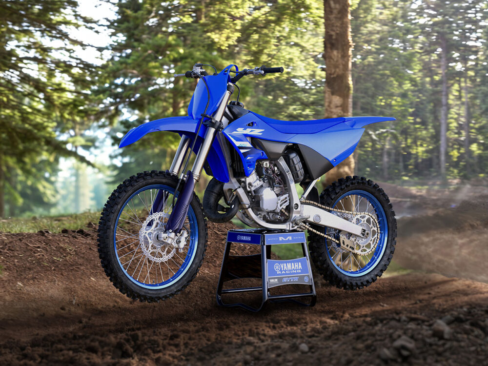 A 2025 YAMAHA YZ125 dirt bike, in blue, is elevated on a stand along a forest trail, surrounded by trees with sunlight filtering through the foliage.