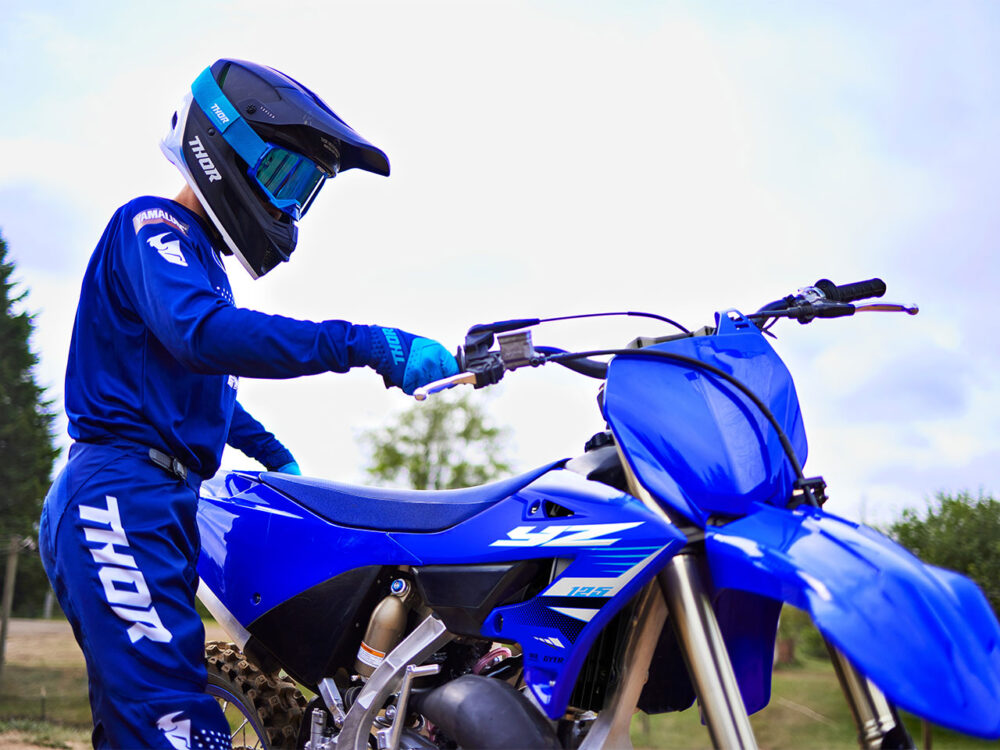 A person in blue motocross gear stands beside a YAMAHA YZ125 2025 bike, gripping the handlebar.