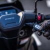 A gloved hand holds a key fob near a motorcycle handlebar with "CFMOTO 150SC" visible on the display screen.