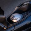 A silver helmet with a brand logo is placed inside the storage compartment of the CFMOTO 150SC motorcycle, alongside black gloves.