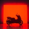 CFMOTO 150SC motorbike silhouetted against a vibrant red rectangular light.