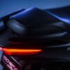 Close-up of the CFMOTO 150SC's rear showcases sleek black seating and bright red taillights, set against a blurred blue background.