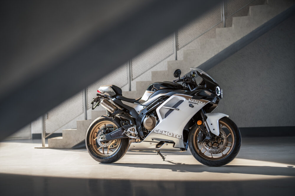 A black and white CFMOTO 500SR VOOM sport motorcycle is parked indoors beside a staircase, with natural light brightening the scene.
