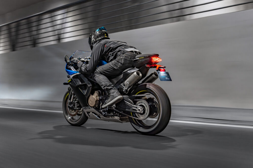 A motorcyclist in black gear rides the CFMOTO 500SR VOOM sport bike at speed through a tunnel, leaning forward with the rear brake light illuminated.