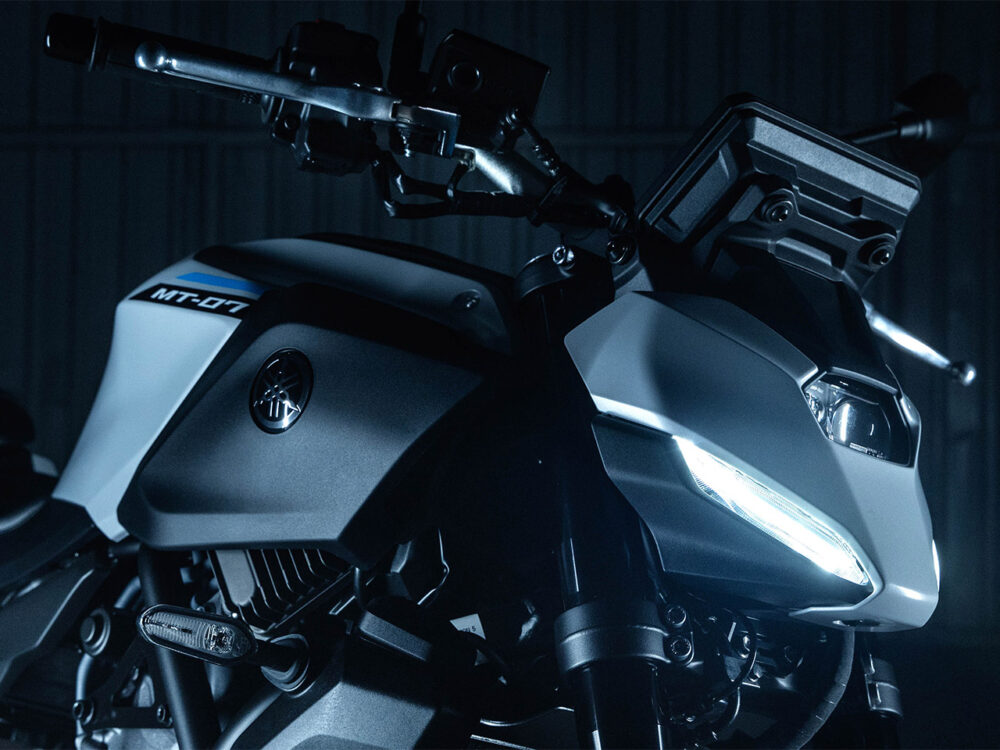 The image showcases a close-up of the YAMAHA MT-07 HO Y-AMT's front section, featuring its handlebars, headlight, and visible emblem. The lighting accentuates its sleek design and metallic finish.