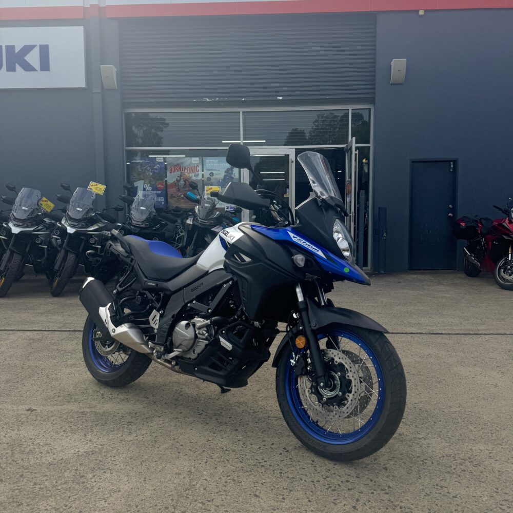 A SUZUKI V-STROM 650XT - DEMO (LAMS) motorcycle in blue and black is parked outside a dealership, with Suzuki and Yamaha signs visible in the background.