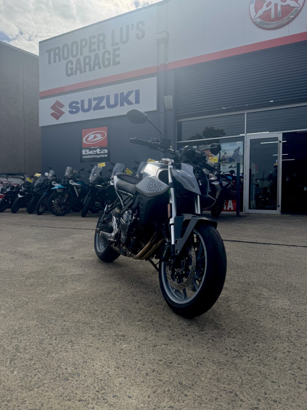 A SUZUKI GSX-8S DEMO is parked outside a dealership, with Suzuki and Beta Motorcycles signs displayed on the building.