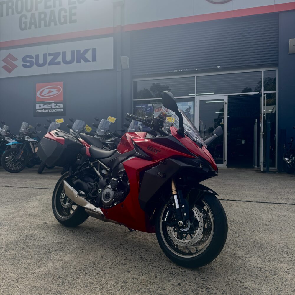 A SUZUKI PANORAMA GT - DEMO sport touring motorcycle in red is parked outside a dealership featuring Suzuki, Beta, and Yamaha branding.